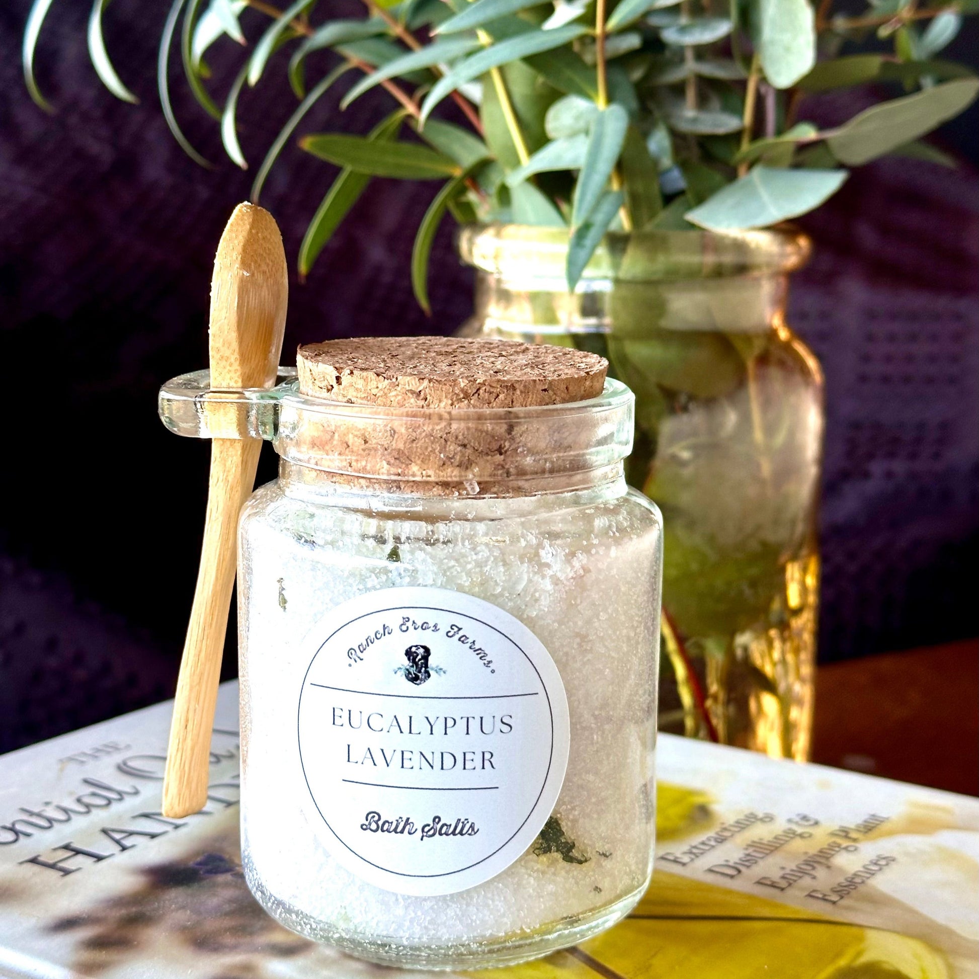 Eucalyptus lavender bath salts in glass jar with wooden spoon. Eucalyptus bouquet in background.